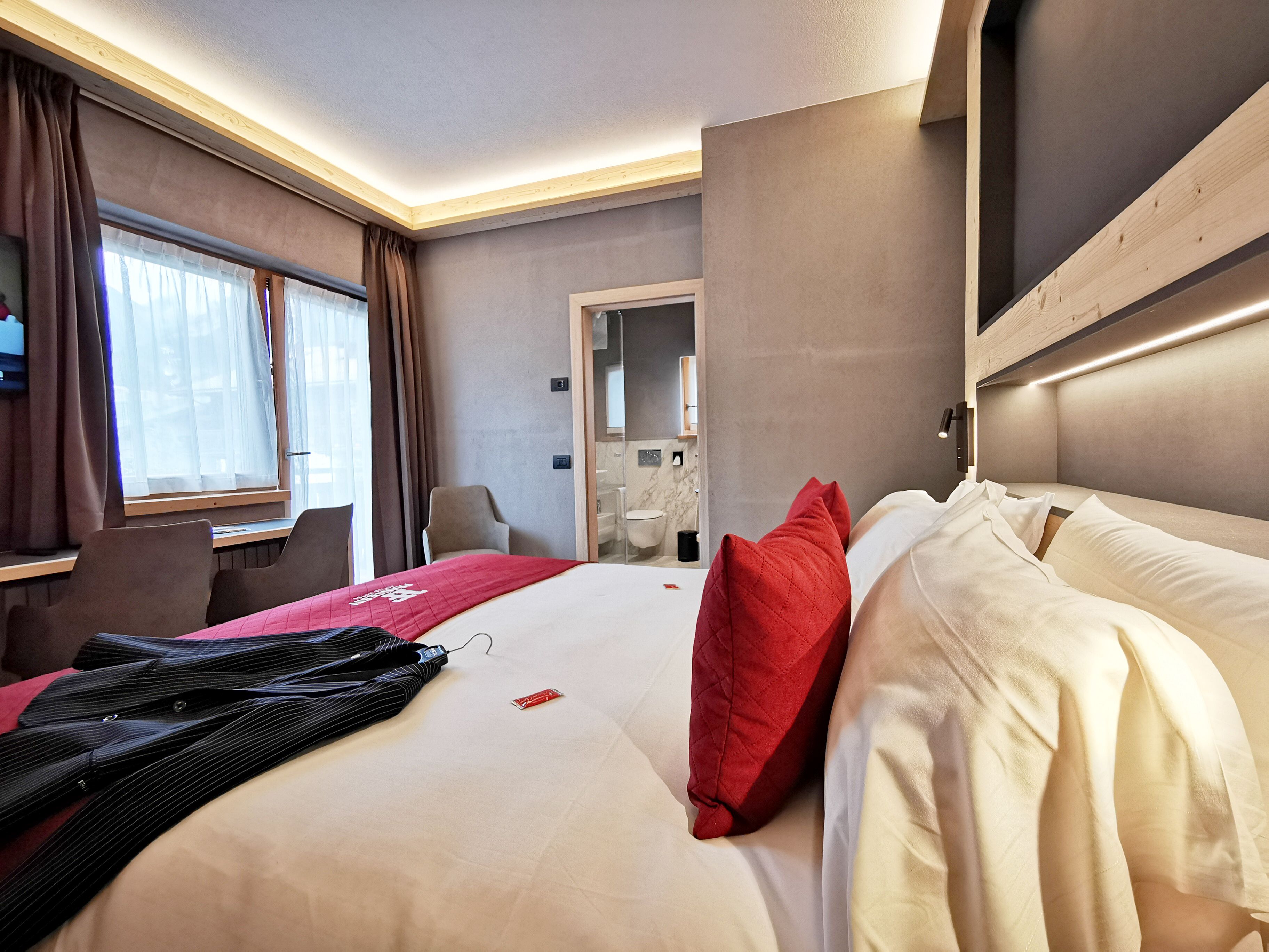 A hotel room with a bed, a desk, a chair, and a bathroom visible through an open door.