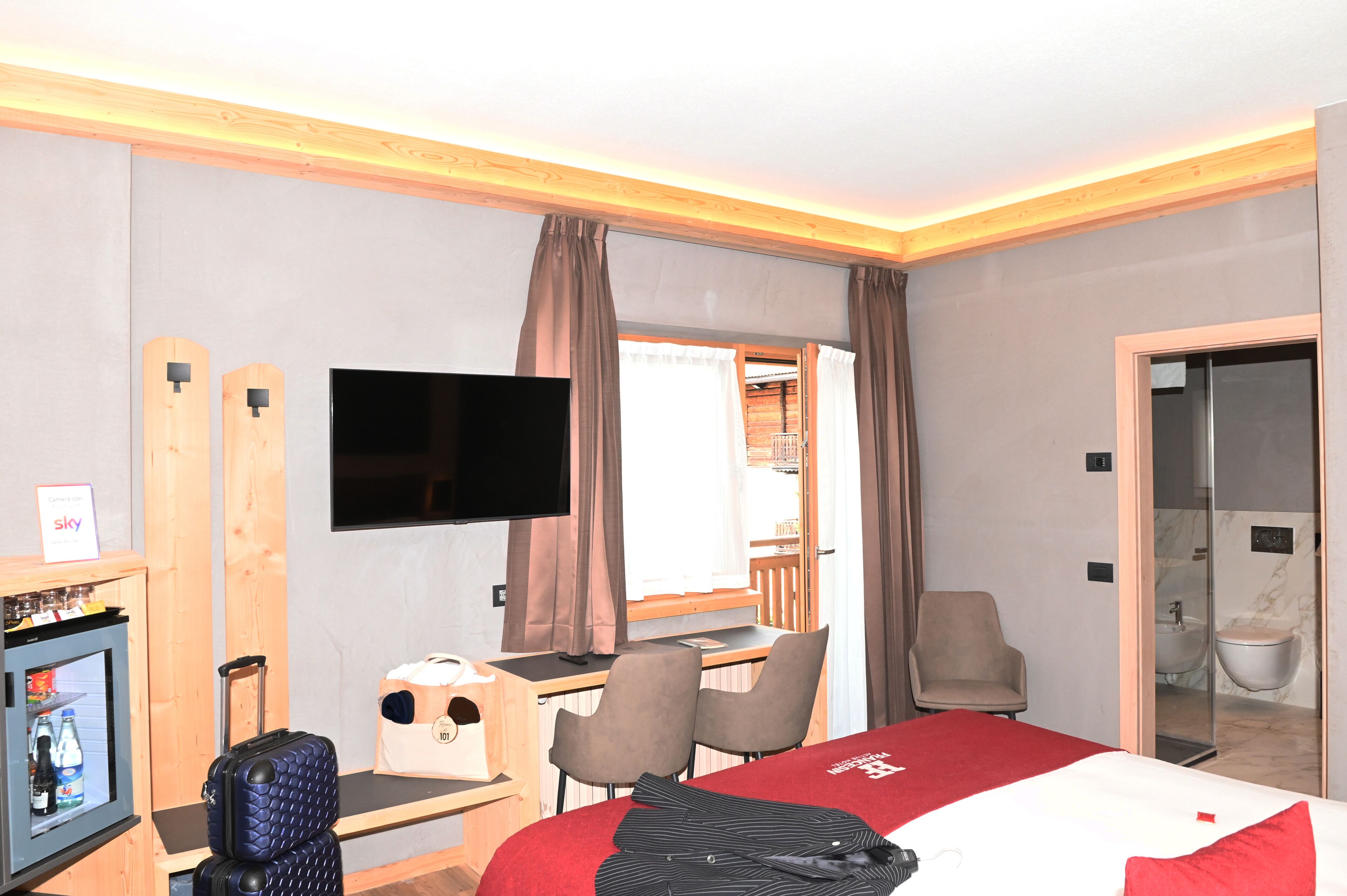 A hotel room with a bed, desk, chair, TV, and a small refrigerator.