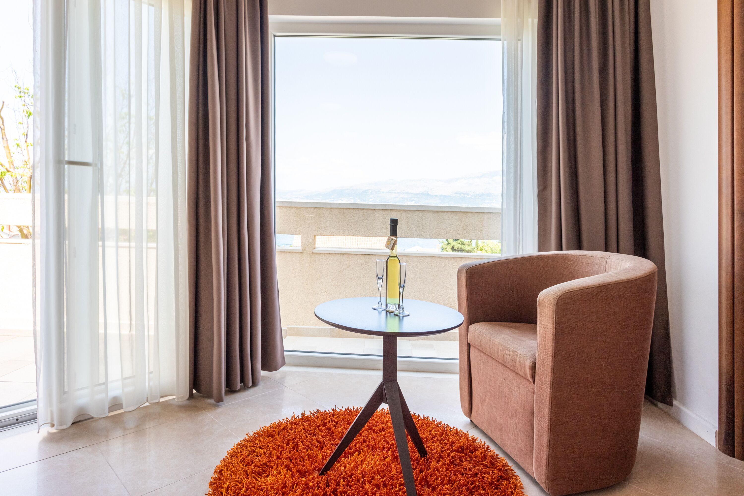 A modern room with a round table, a brown armchair, and a view of mountains through large windows.