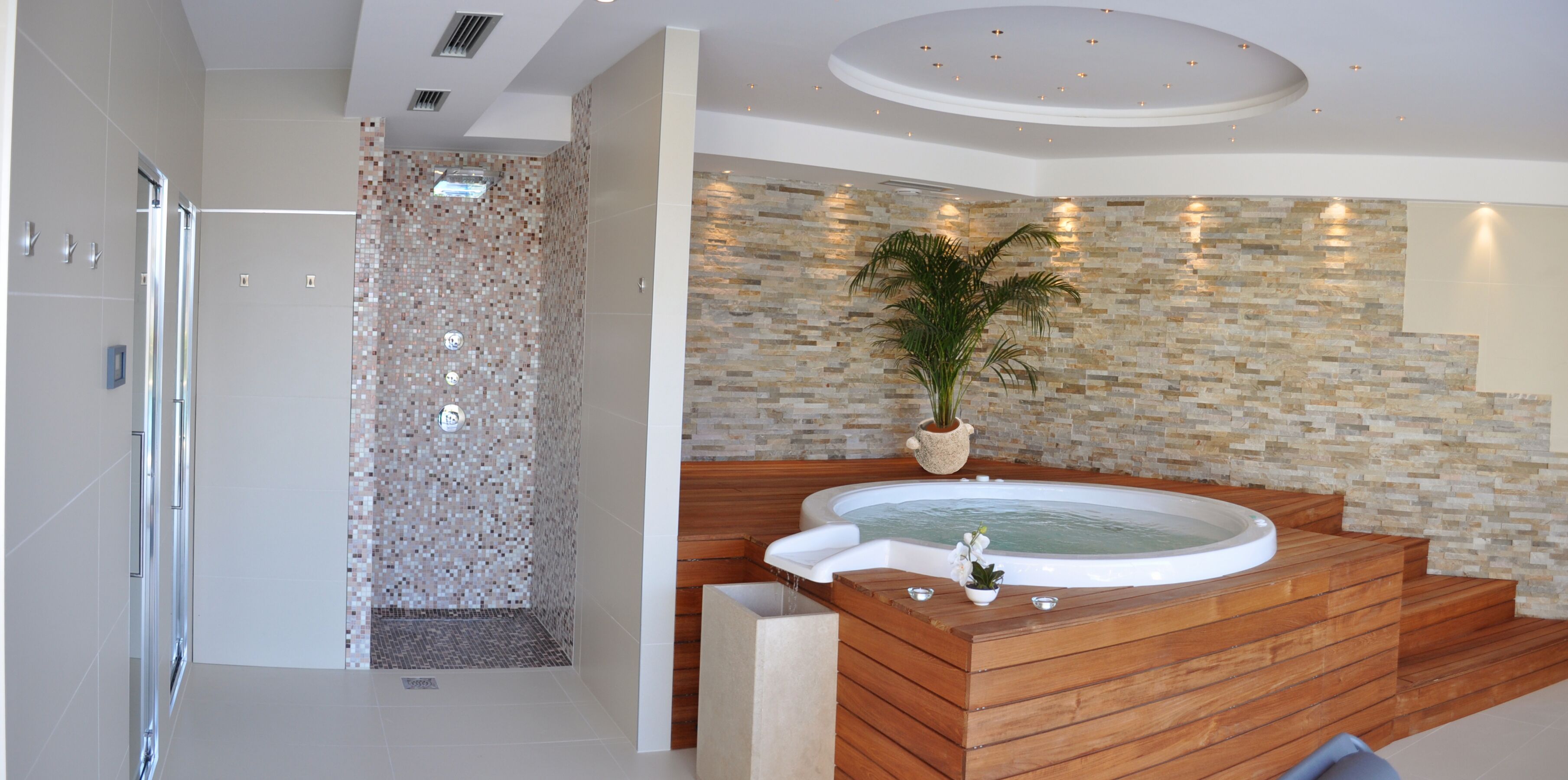 A modern bathroom with a shower, a wooden bathtub, and a mosaic wall.