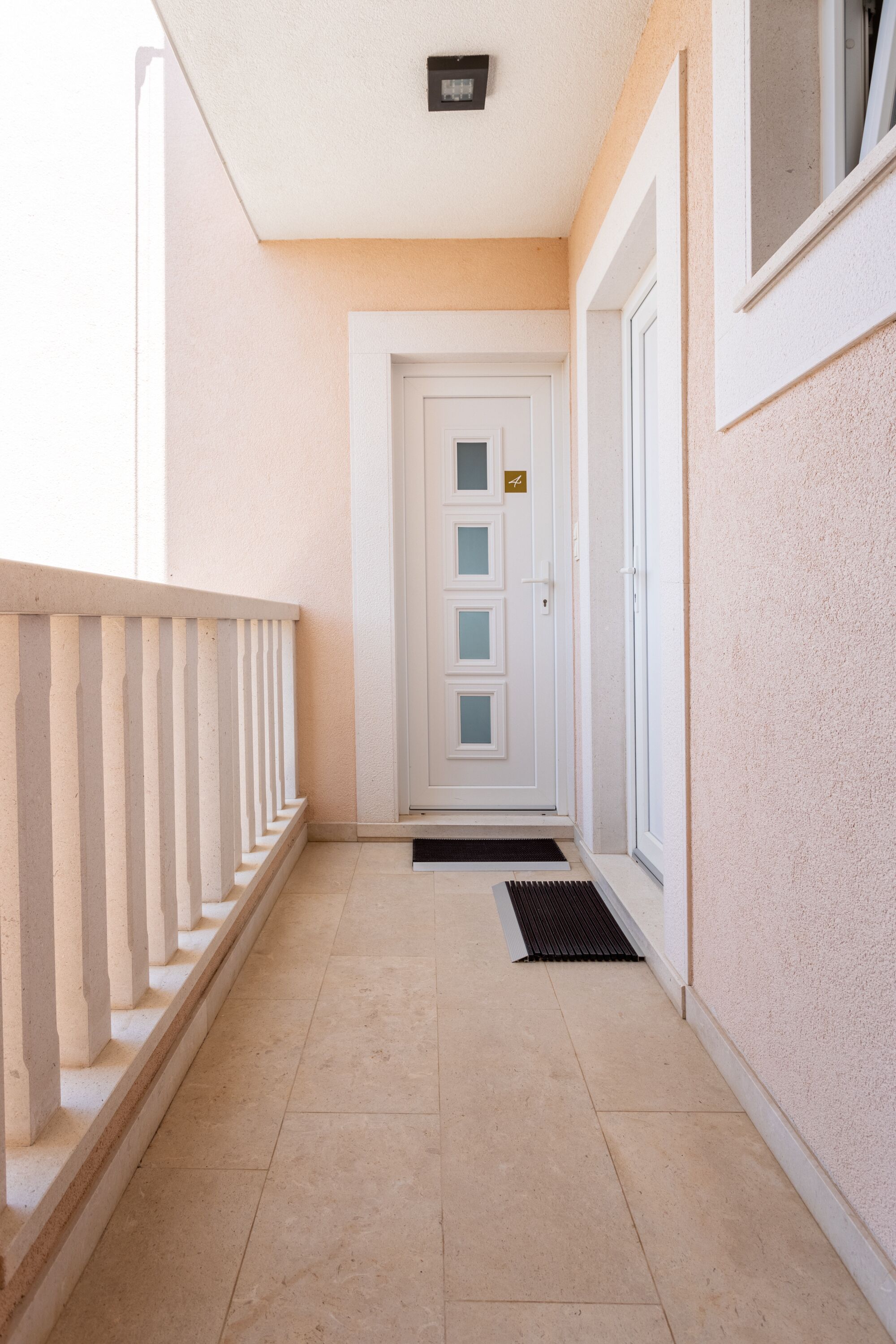 A hallway with a white door, a small window, and a metal doormat.