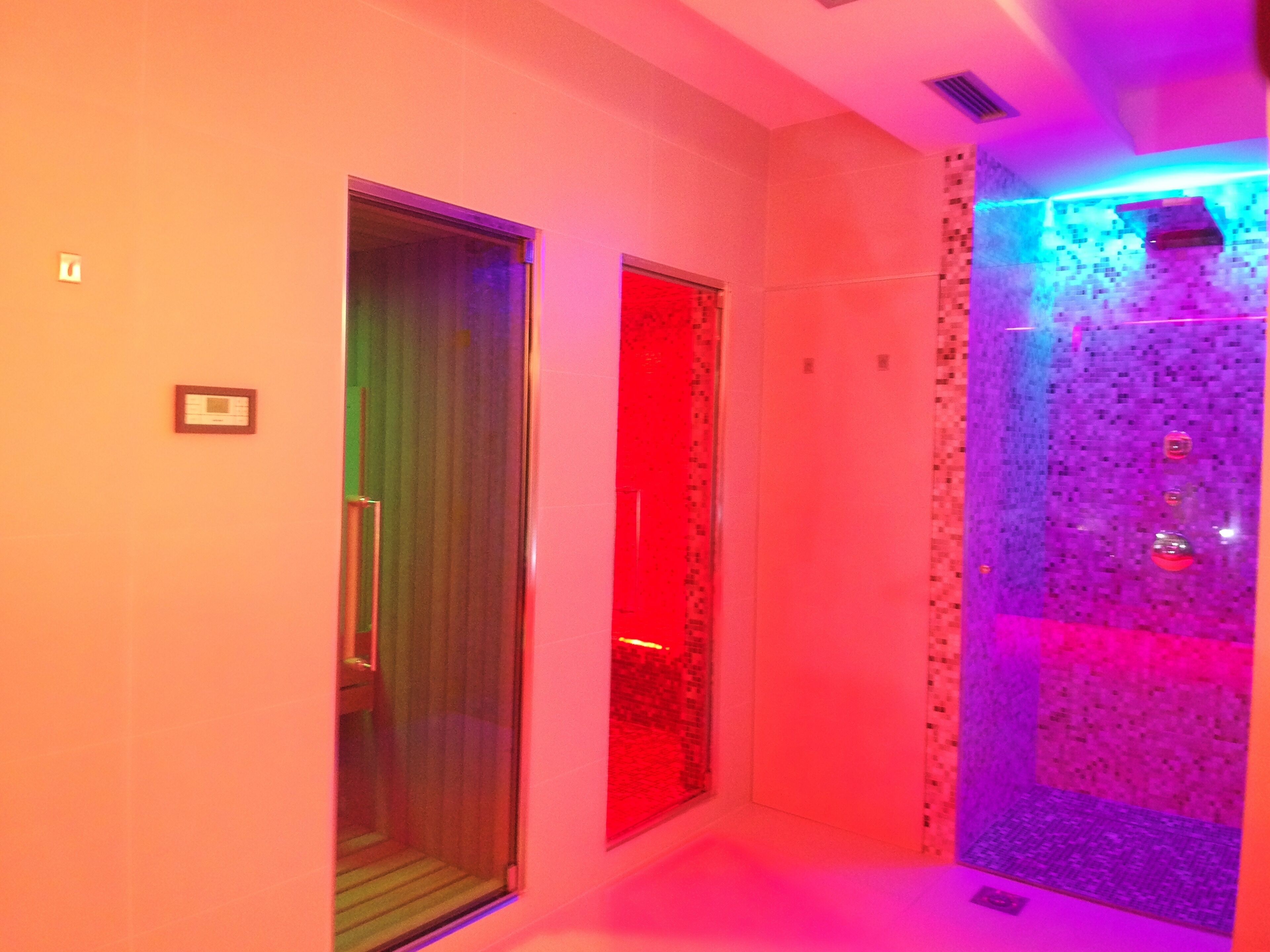 A hallway with a glass door, a red-lit wall, and a tiled wall with a blue light.