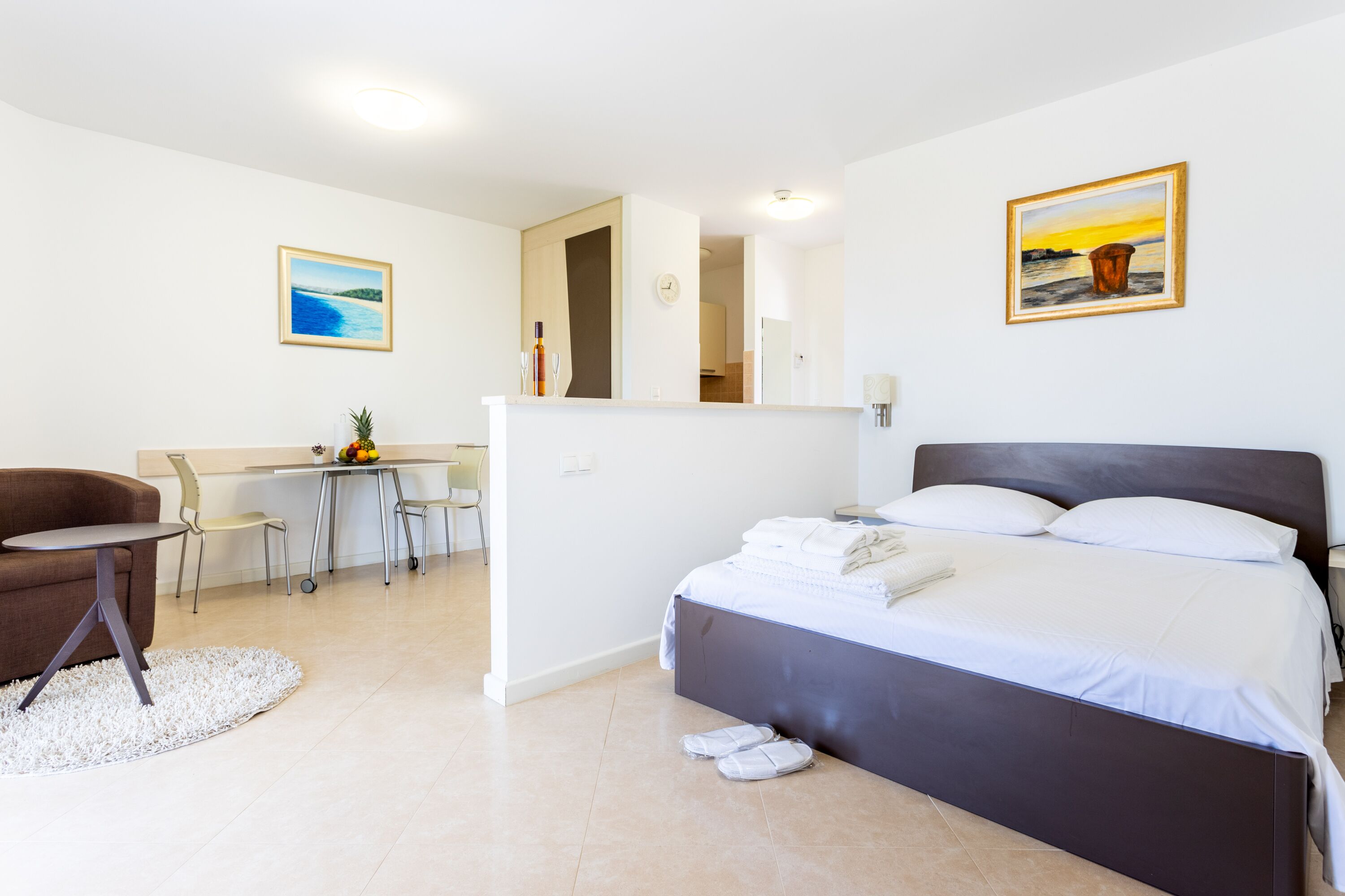 A modern hotel room with a bed, a desk, a chair, and a painting on the wall.