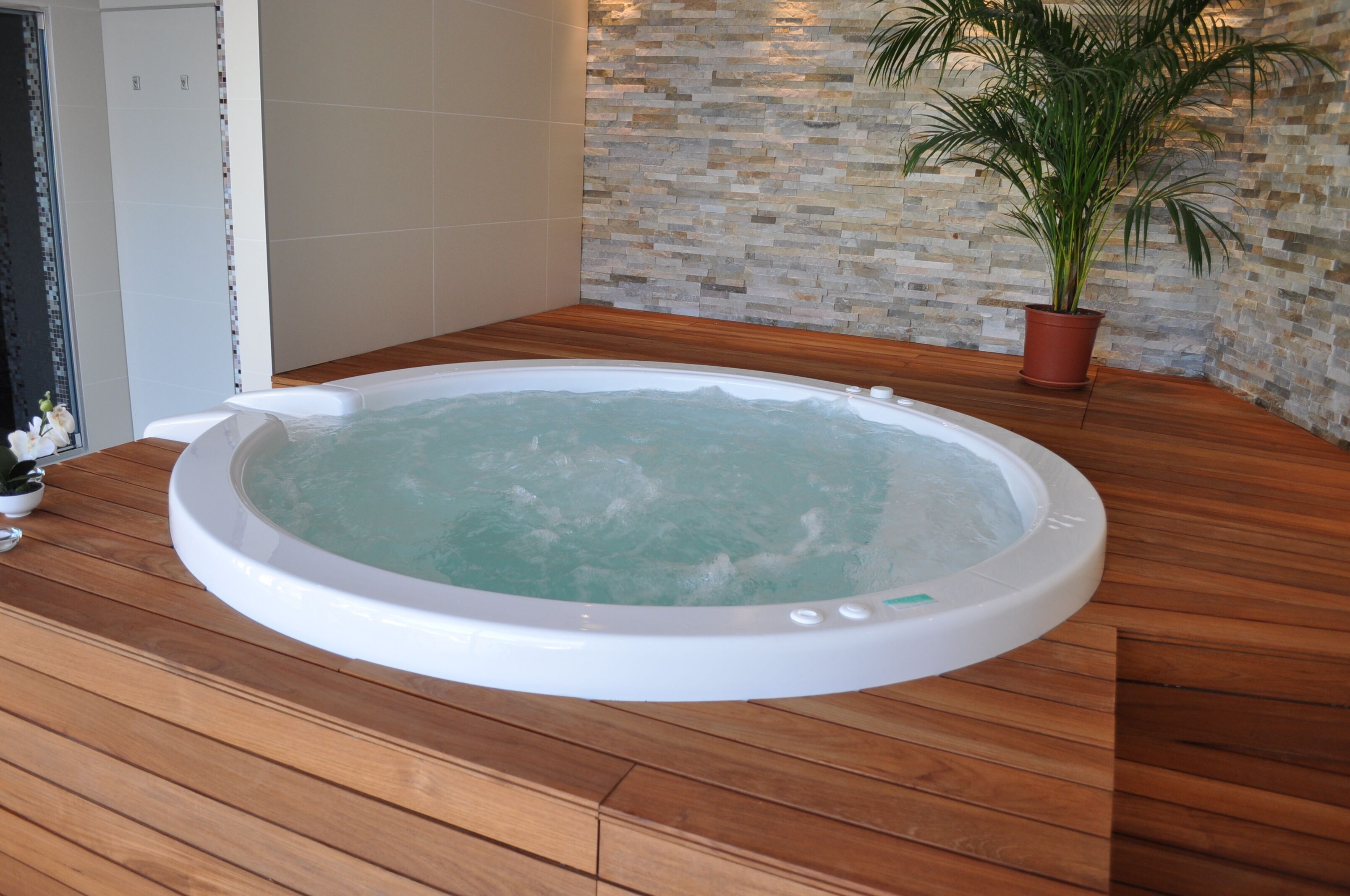 Un bain à remous dans une pièce dotée d’un plancher en bois et d’un mur en pierre.