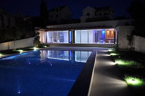 A modern house with a swimming pool, large glass windows, and outdoor lighting.