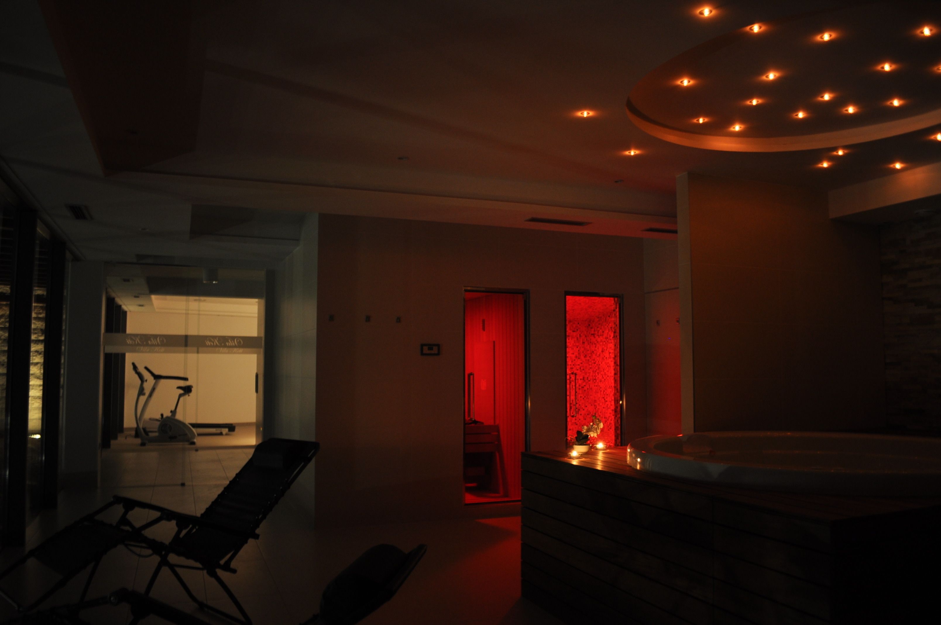 A dimly lit room with a massage table, a small exercise bike, and a red-lit wall.