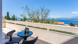 Un balcon avec une table et des chaises, offrant une vue panoramique sur la mer et les montagnes lointaines.