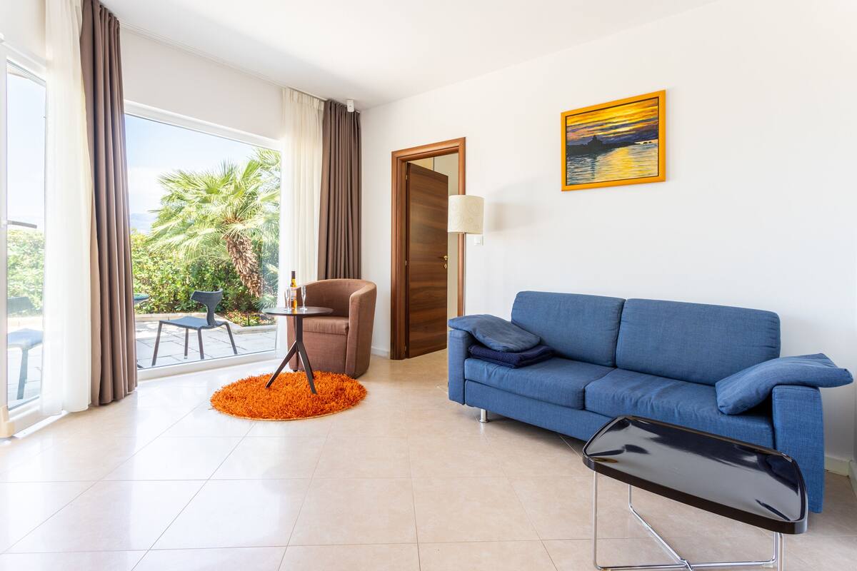 A modern living room with a blue sofa, a small table, and a view of the outdoors.