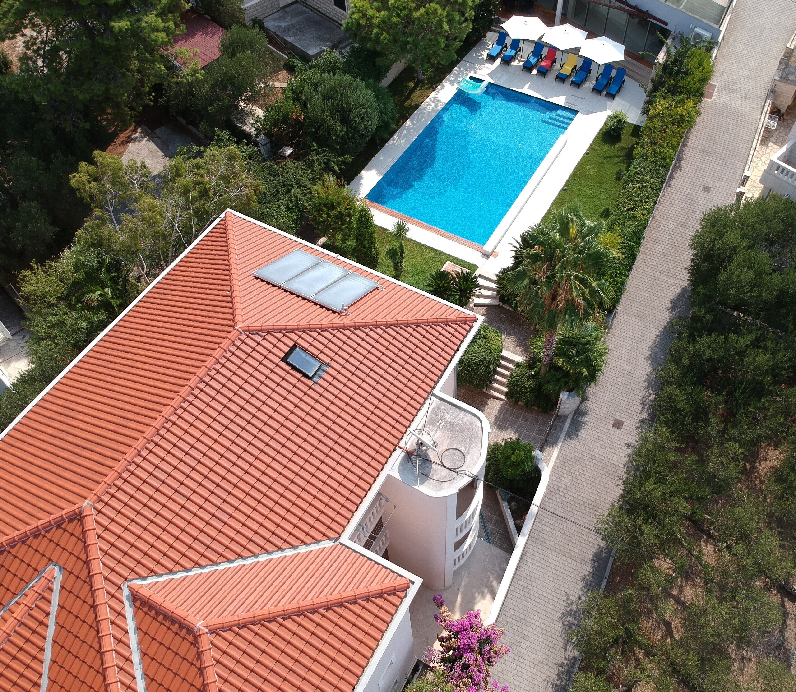 Un immeuble résidentiel avec un toit recouvert de tuiles rouges, une piscine entourée de chaises longues et de verdure.