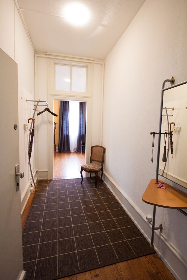 A narrow hallway with a dark patterned rug, a wooden chair, and a mirror on the right wall.