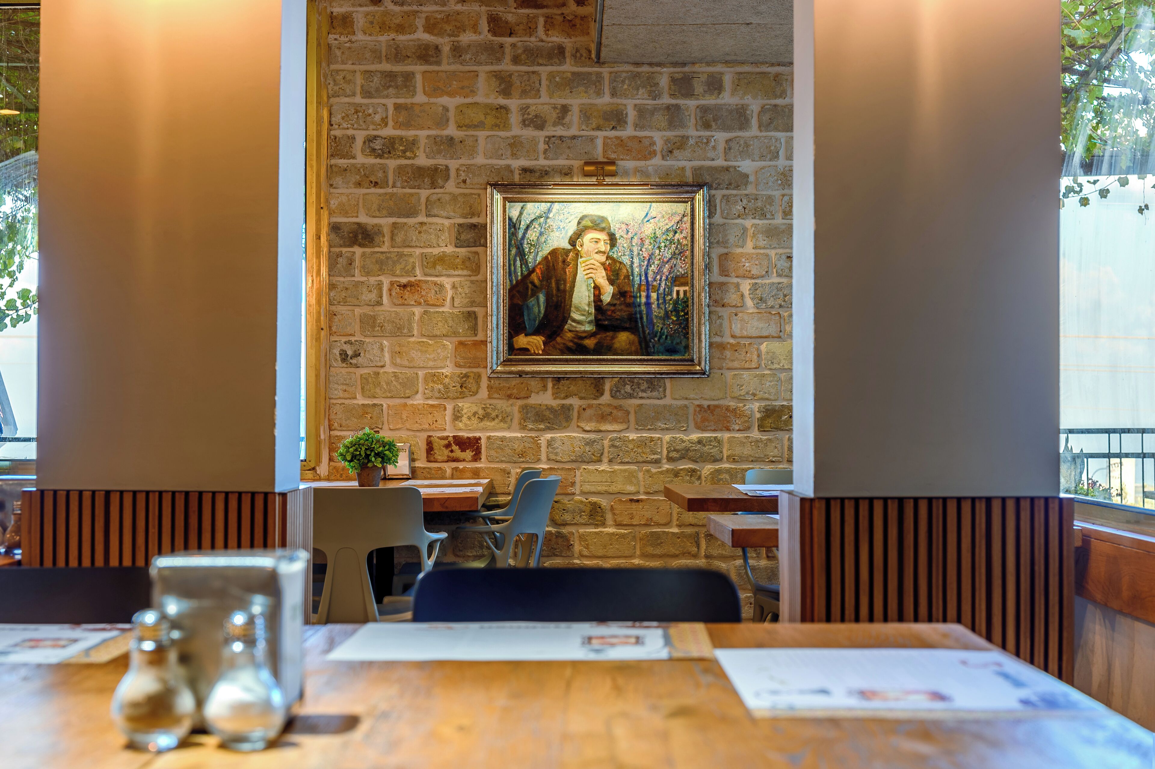 Restaurante com parede de tijolos, mesas e cadeiras de madeira.
