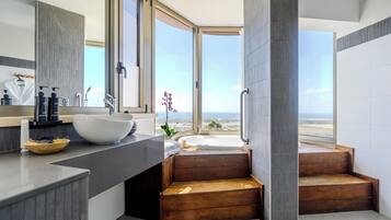 A modern bathroom with a large window, a white sink, and wooden steps leading to a jacuzzi.