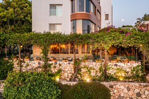 Un edificio moderno con un muro de contención de piedra y un área de estar al aire libre cubierta, con luces colgantes.