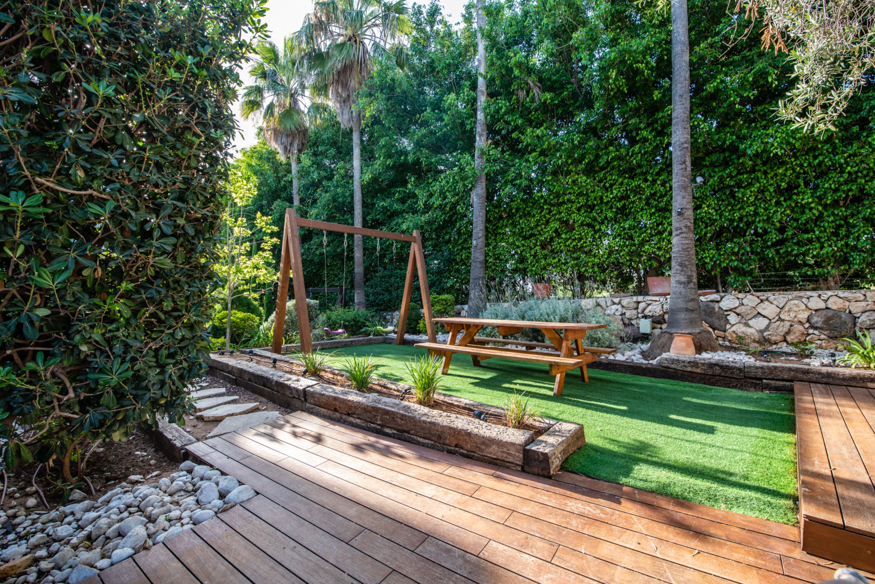 A wooden deck with a swing set, picnic table, and stone wall.
