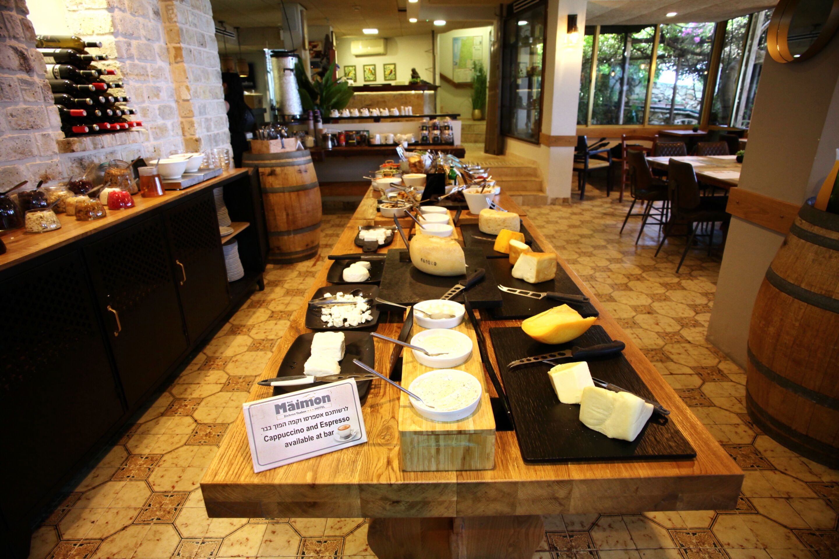 A buffet with various cheeses, meats, and condiments. There is a sign indicating the availability of cappuccino and espresso at the bar.