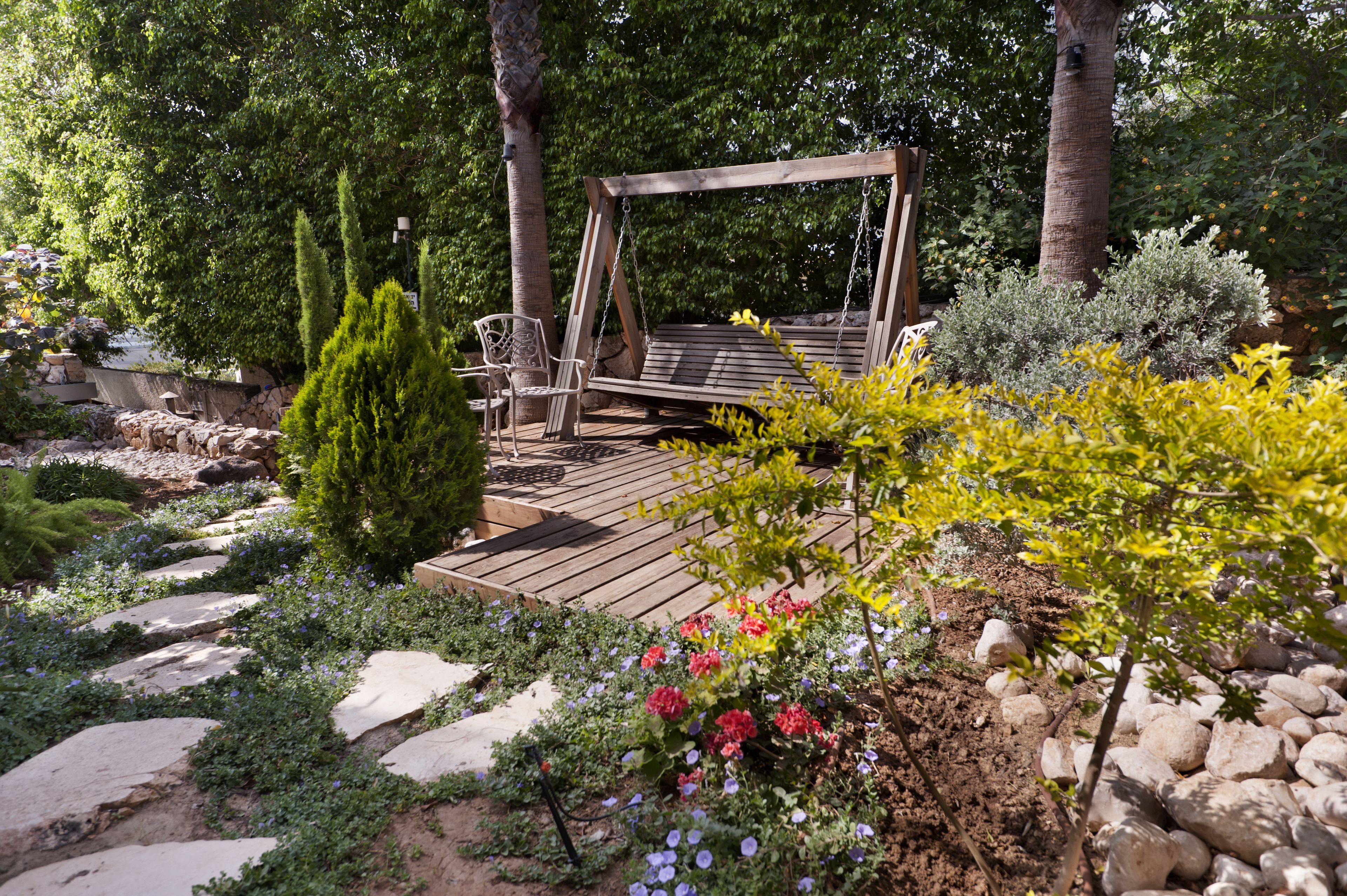 Een houten schommelset in een tuin met stenen paden en verschillende planten.