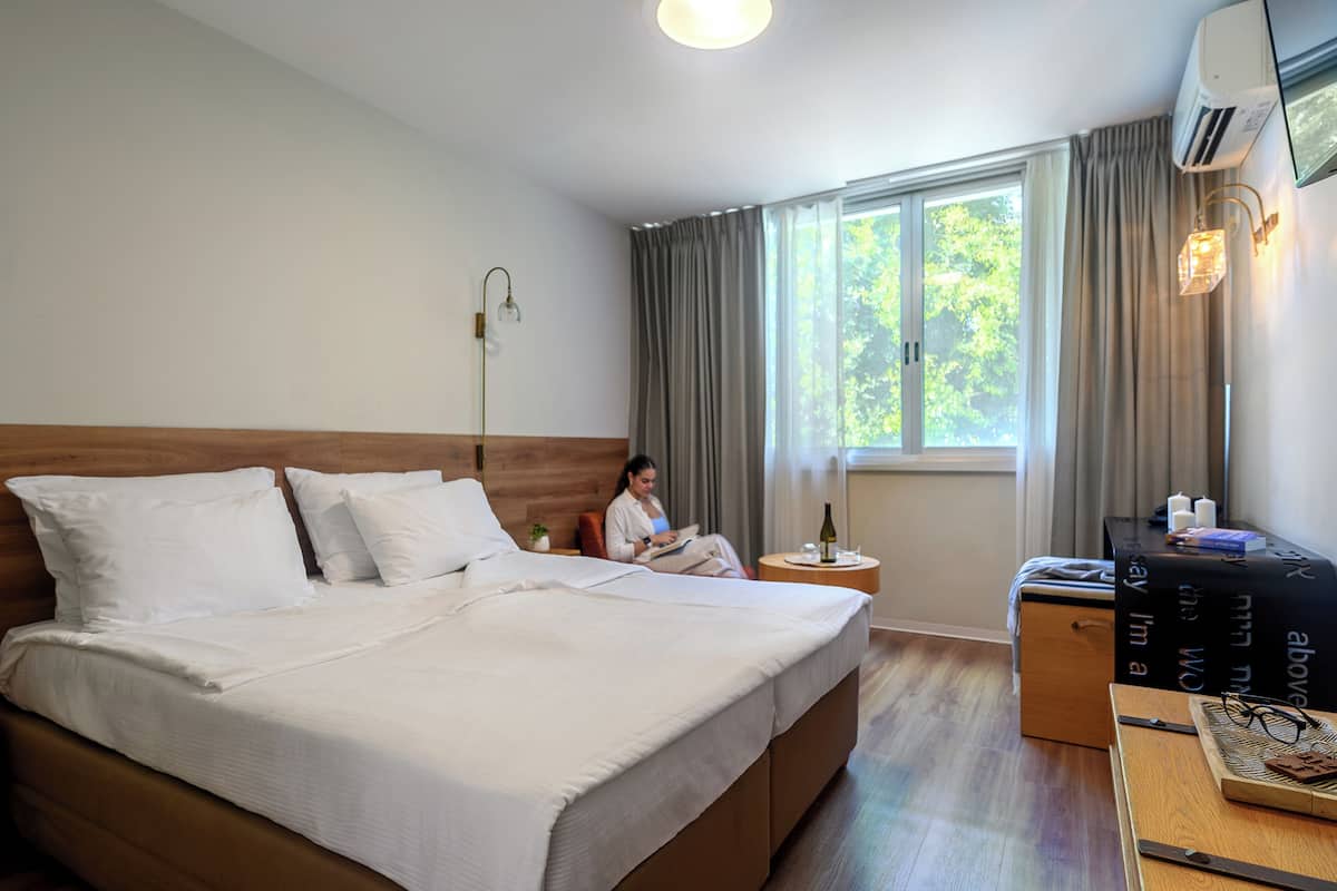 Habitación de hotel con una cama grande, una mesita de noche con lámpara, un escritorio con silla y una ventana con cortinas.