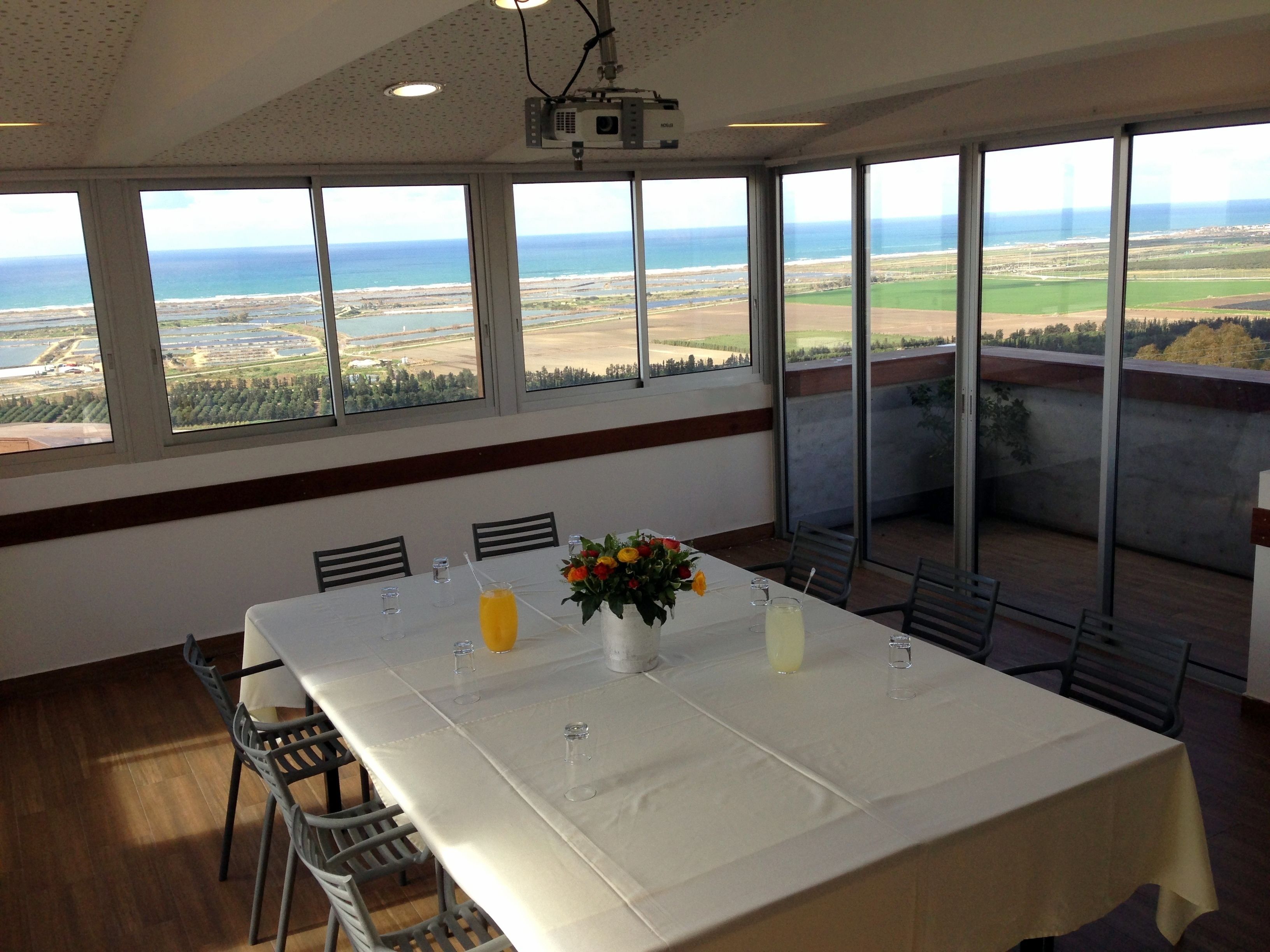 A dining area with a table set for four, large windows offering a view of the ocean and landscape, and a ceiling-mounted projector.