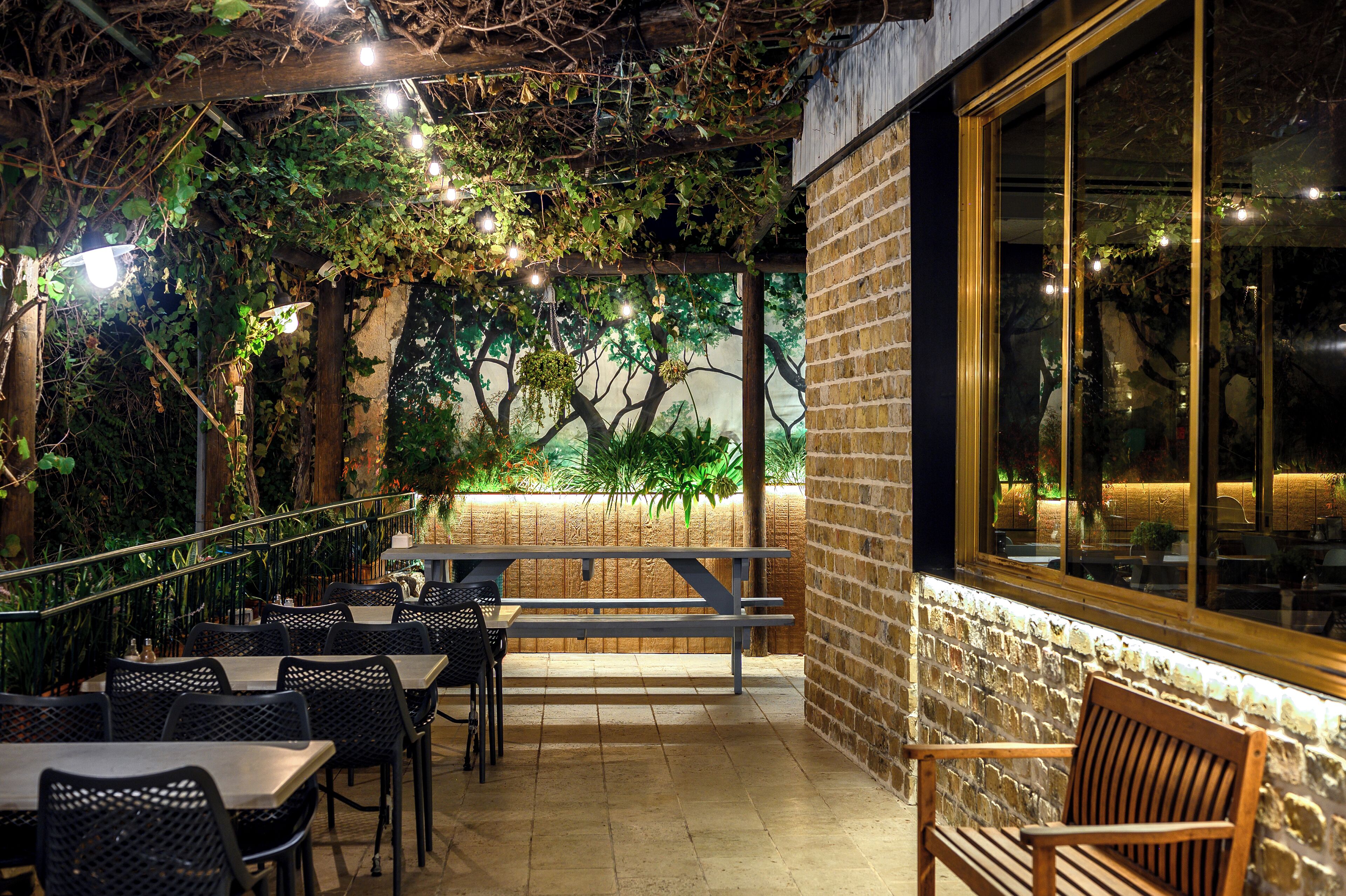 An outdoor patio with tables and benches, surrounded by brick walls and greenery.