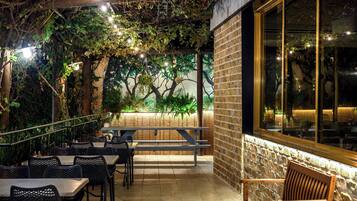 An outdoor patio with tables and benches, surrounded by brick walls and greenery.