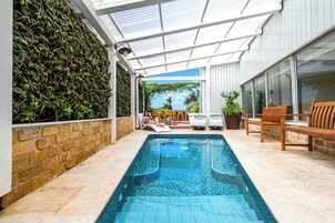 Una piscina con plataforma de baldosas, un porche cubierto y un muro de ladrillo con plantas trepadoras.