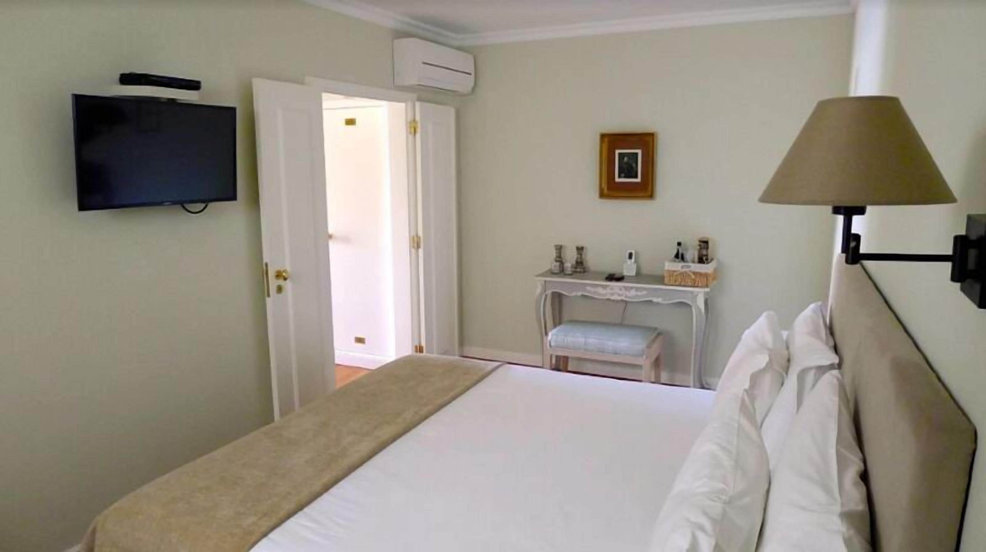 A hotel room with a bed, a television mounted on the wall, a desk with a chair, and a lamp.