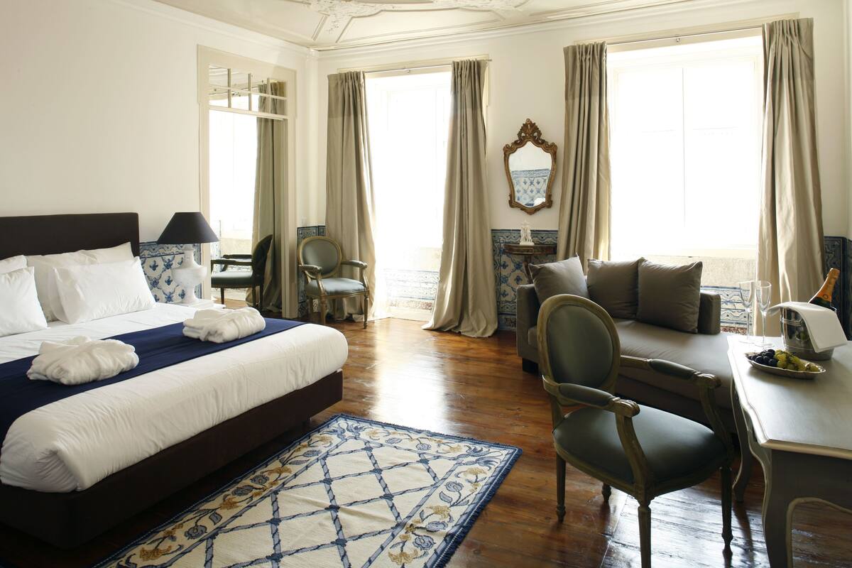 A hotel room with a large bed, a desk, a chair, and a view of the sea.