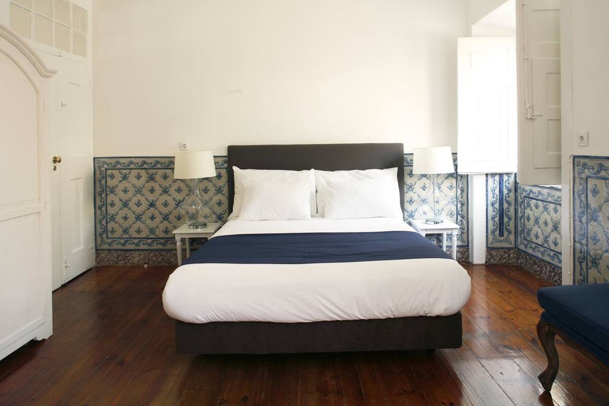 A bedroom with a large bed, two bedside tables with lamps, and patterned wallpaper.