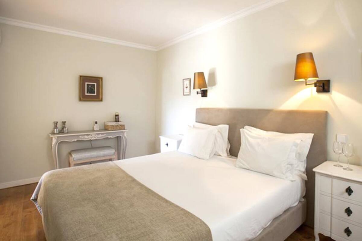 A hotel room with a bed, bedside tables, a nightstand, a lamp, a framed picture, and a fireplace.