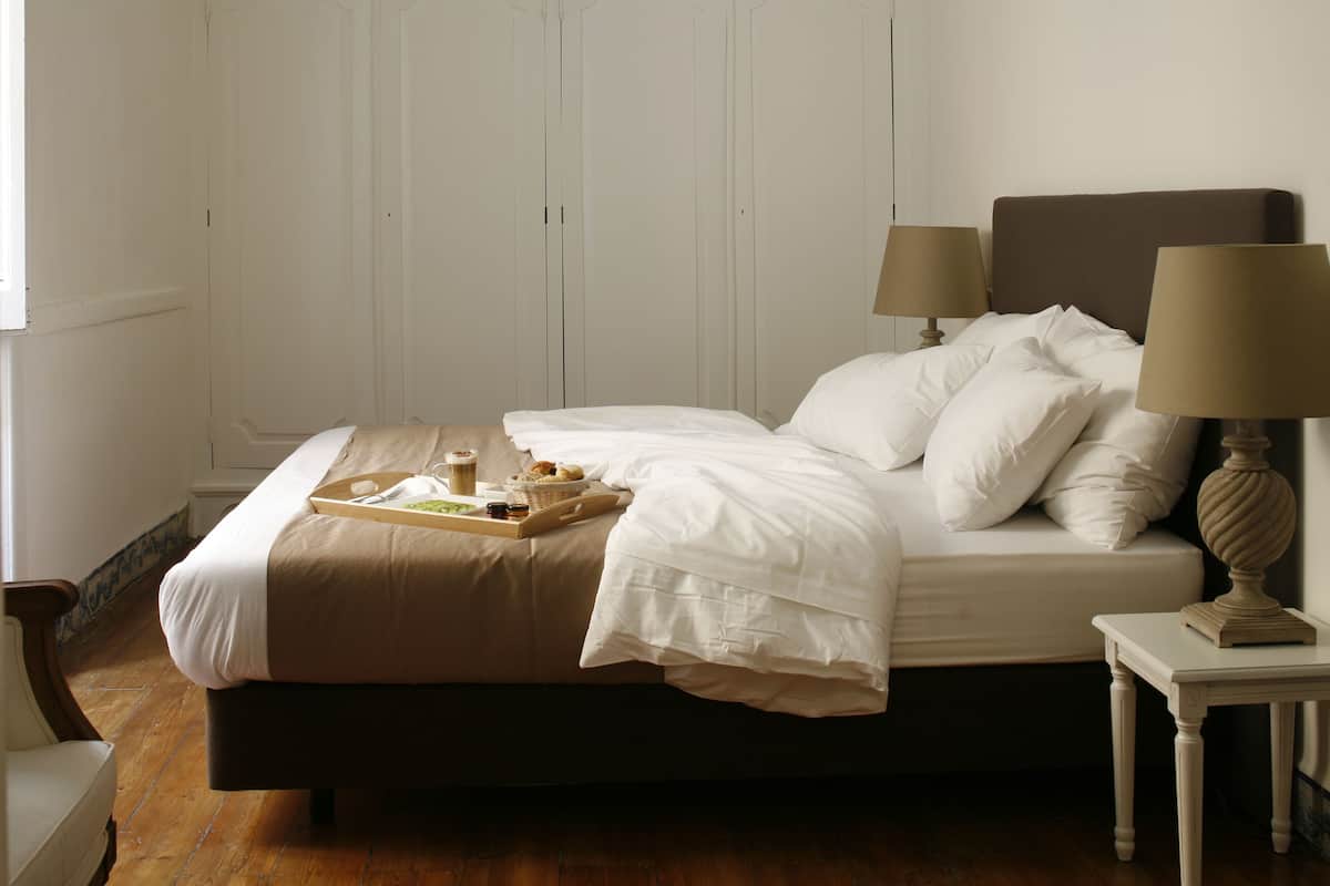 A neatly made bed with white linens, a tray with breakfast items, and two bedside lamps.