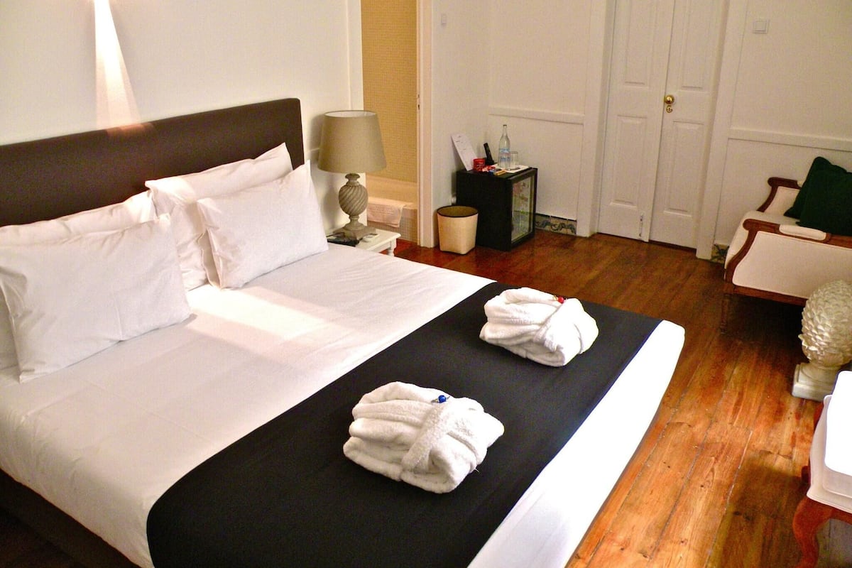 A hotel room with a bed, a nightstand, a lamp, a small table with toiletries, and a door.