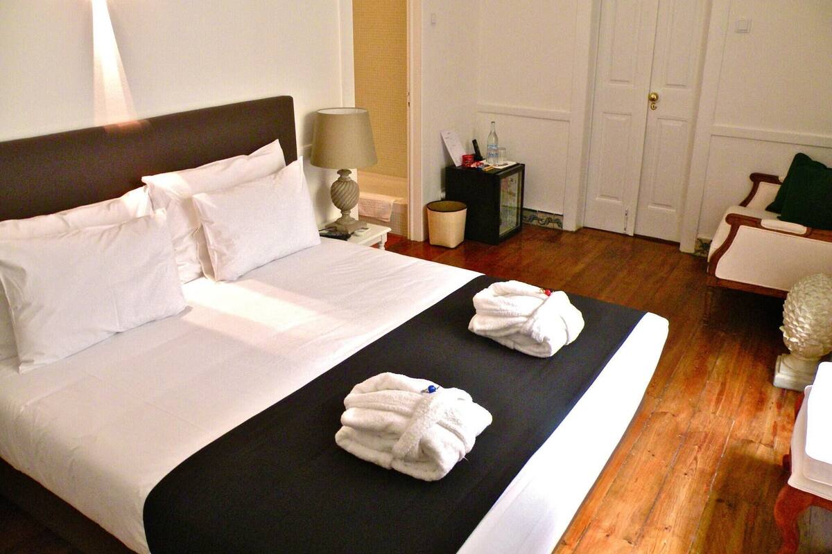 A hotel room with a bed, a nightstand, a lamp, a small table with toiletries, and a door.