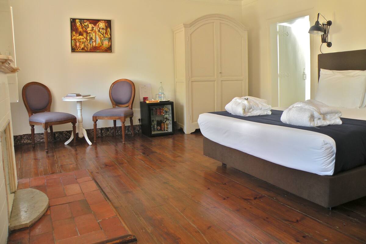 A hotel room with a bed, two chairs, a small table, a cabinet, and a painting on the wall.
