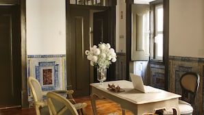 A dining area with wooden flooring, a white table, and two chairs. A vase with flowers is on the table. - Palacio Ramalhete (Lisbon)