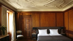 A classic room with a large bed, wooden paneling, a chair, a dresser, and a desk with a lamp. - Palacio Ramalhete (Lisbon)