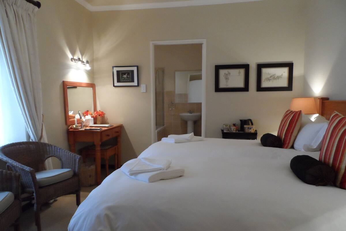 Una camera d'albergo con un letto grande, una scrivania con una sedia, uno specchio e due quadri appesi al muro.