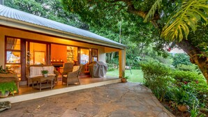 A covered outdoor seating area with stone flooring, wicker furniture, and a bookshelf. - Porcupine Ridge Guest House (Sabie)
