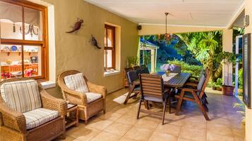 Un patio acogedor con muebles de mimbre, una mesa de comedor y vistas a un jardín exuberante a través de una ventana.