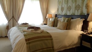 A hotel room with a large bed, two bedside tables, a headboard, and a window with curtains. - Porcupine Ridge Guest House (Sabie)