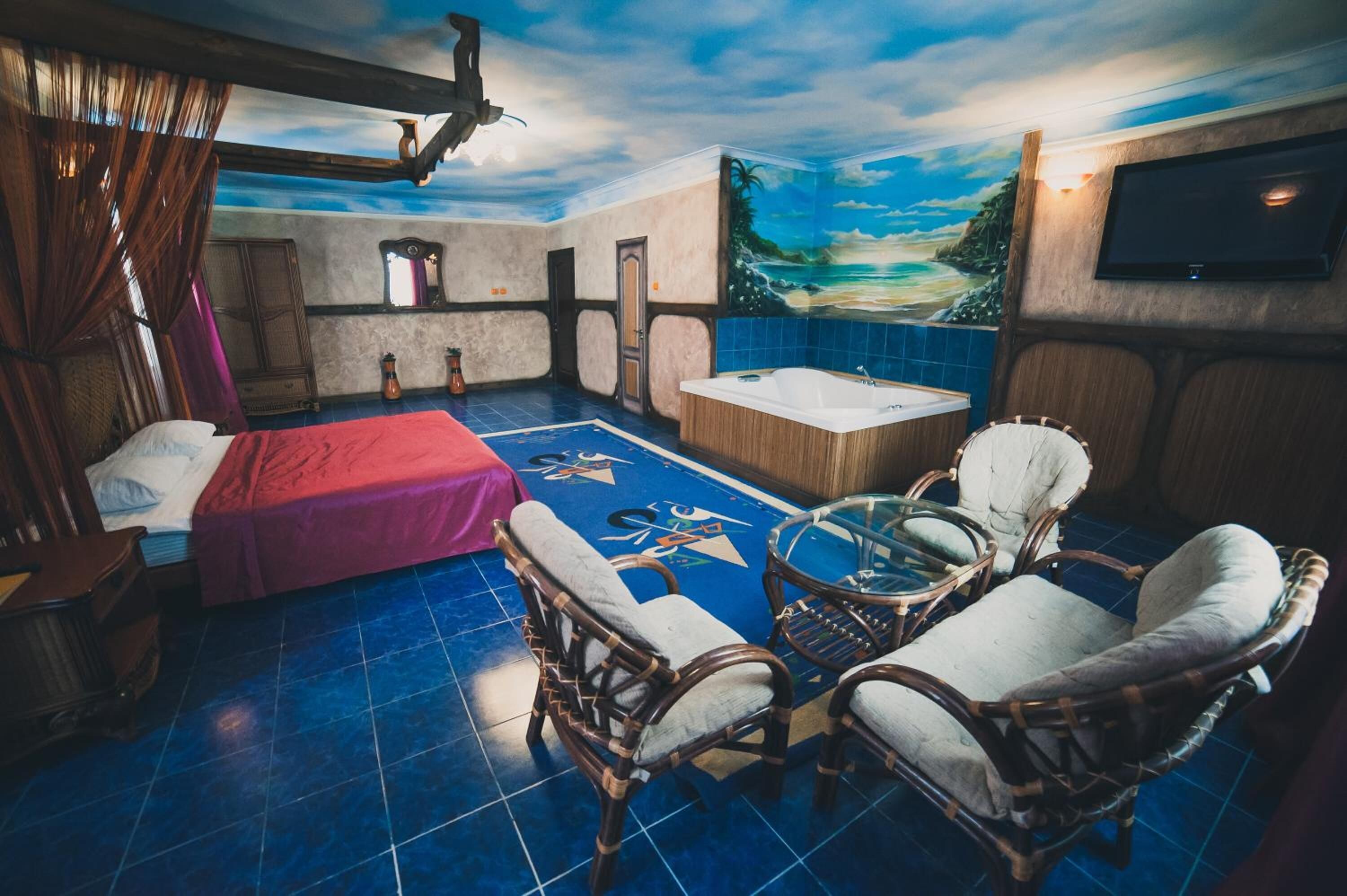 A room with a bed, a bathtub, wicker chairs, and a mural of a beach scene.