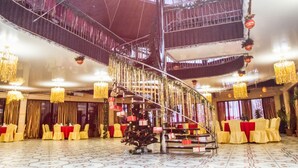 Un gran salón con una escalera central, decoración roja y dorada, y candelabros.