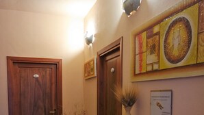 Un corridoio con porte in legno, una reception, un vaso con piante secche e opere d'arte appese al muro.