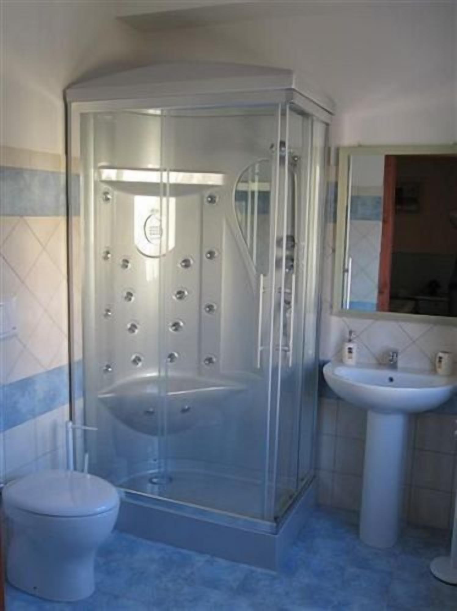 A bathroom with a glass-enclosed shower, a toilet, and a sink with a mirror above it.