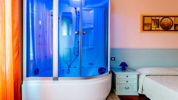 Una stanza con cabina doccia in vetro, un comodino con lampada e un letto con copripiumino a fantasia.