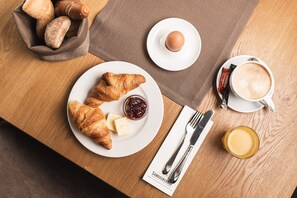 A breakfast setting with croissants, a boiled egg, coffee, and a glass of juice on a wooden table. - Samnaunerhof Vital-Hotel (Samnaun)