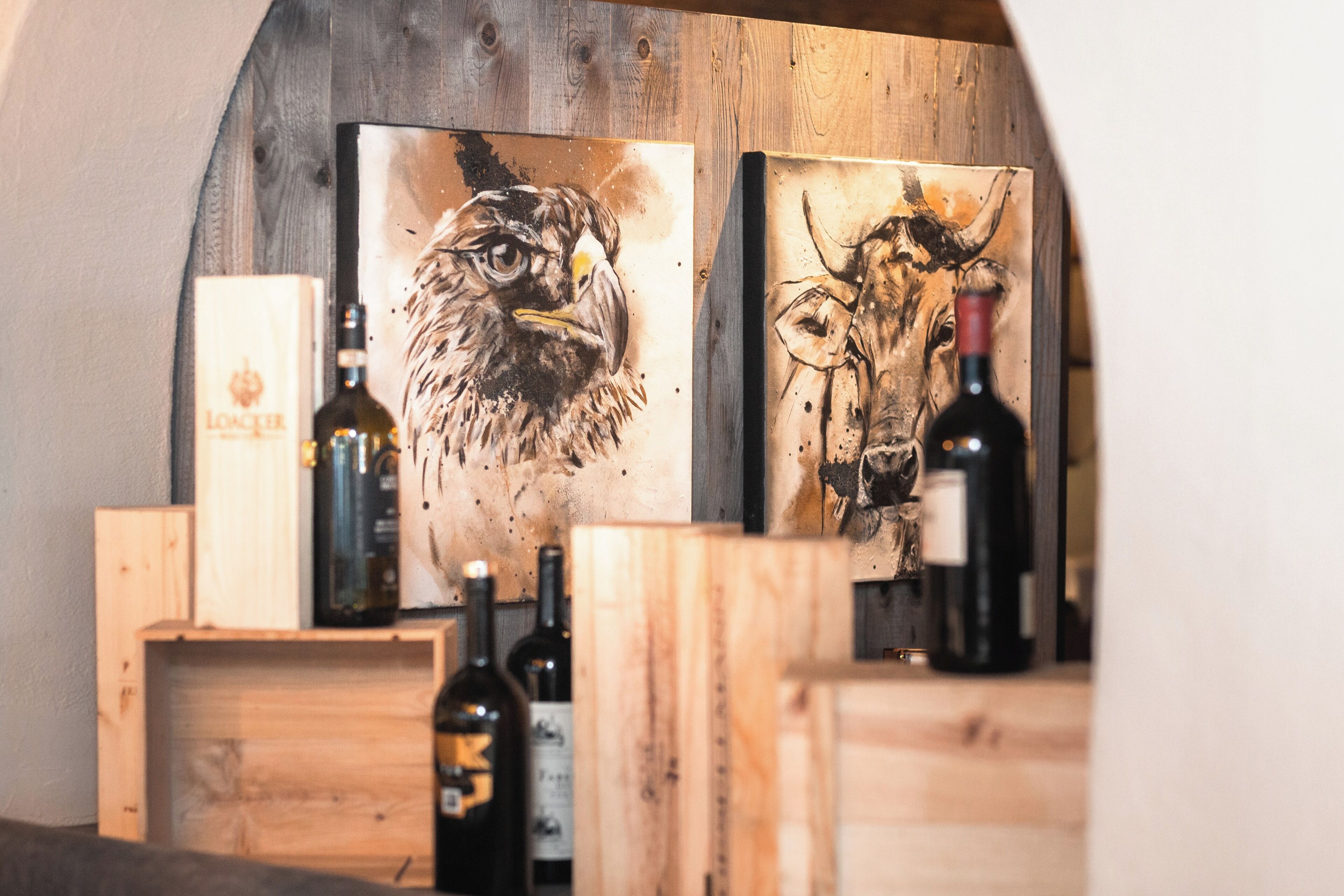 Una estantería de madera para botellas de vino, con botellas y dos cuadros de animales.