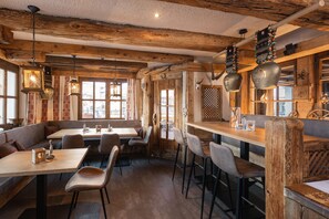 Un interior rústico con vigas de madera, ladrillo visto y decoración tradicional. Se disponen mesas y bancos para comer.