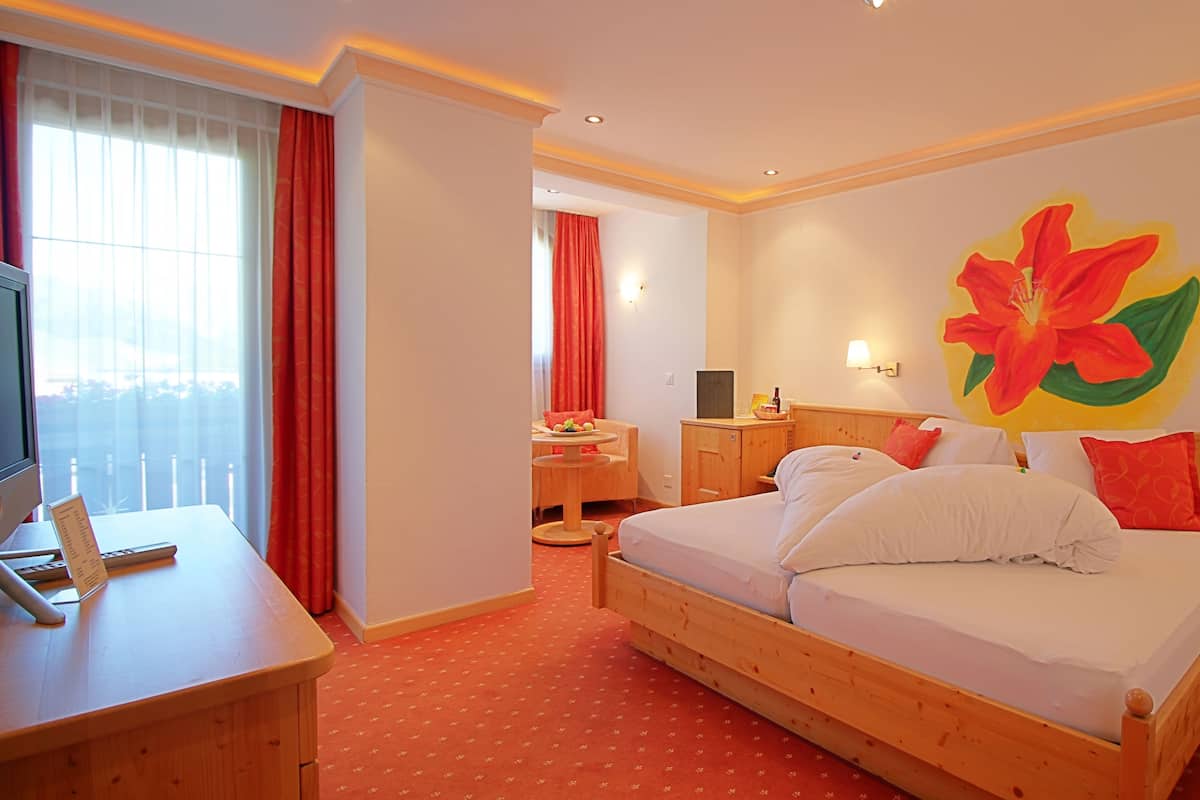 A hotel room with a bed, a desk with a computer, a chair, and a large window with curtains.