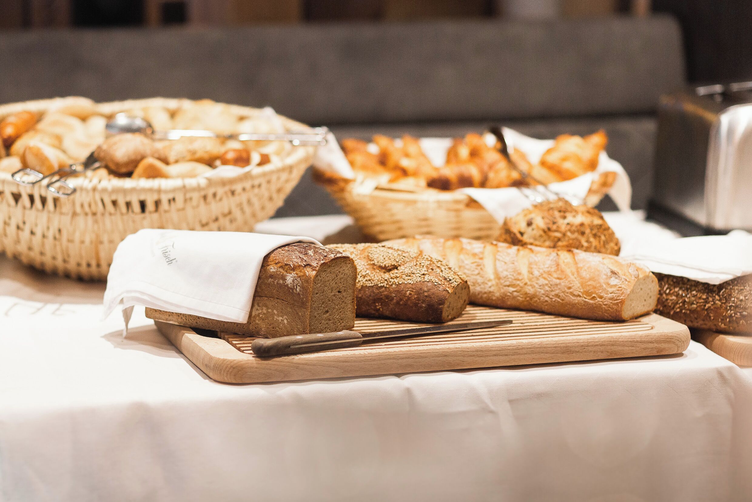 A variety of breads and pastries on a table, with a cutting board and a knife.