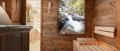 A wooden sauna room with a wooden bench, a wooden wall with a window showing a mountain stream, and a sauna heater.